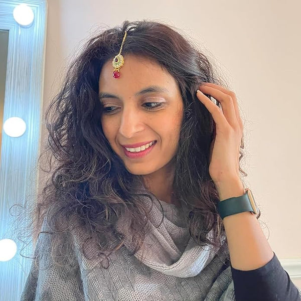 Model wearing a gold-plated Indian maang tikka with Kundan stones and a red glass drop for a bridal look.

