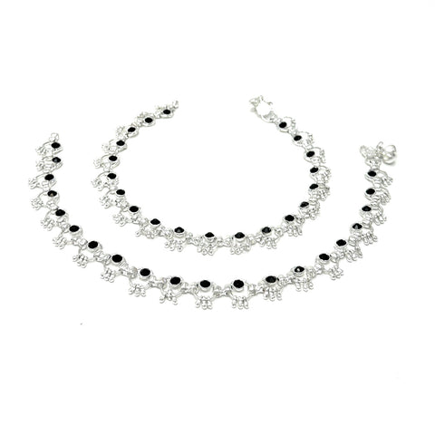 Model wearing silver-plated ring-link anklets with round black stone accents and soft bell chimes.
