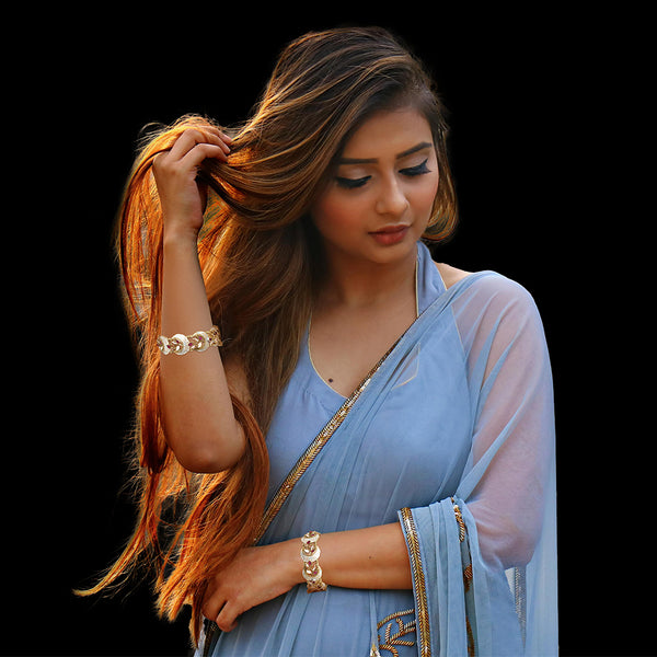 Model wearing gold-tone Meenakari Polki bangles on both wrists with a blue Bollywood saree.
