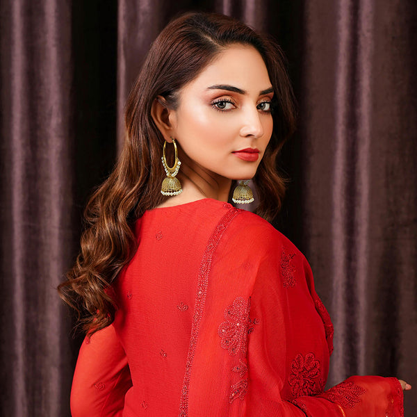 Model wearing gold-plated infinity hoop jhumka earrings with white pearl accents and a red dress.
